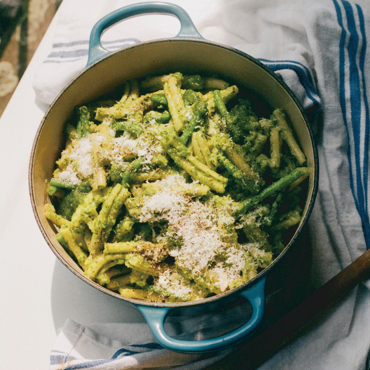A pot of pasta with green sauce and grated cheese.