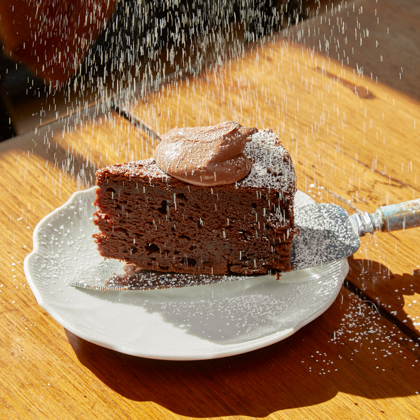 A slice of chocolate cake dusted with powdered sugar on a white plate.