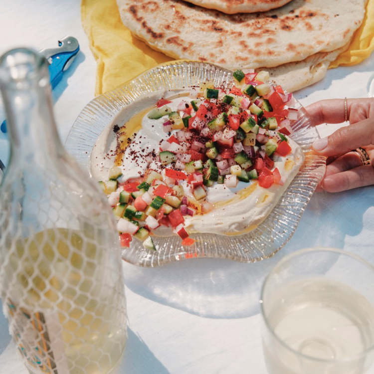 A hand holding a plate of colorful food, with drinks nearby.